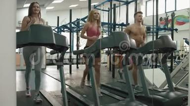 一名<strong>肌</strong>肉发达的男子和两名运动妇女正在现代健身房的<strong>跑步机</strong>上训练。 4K录像。